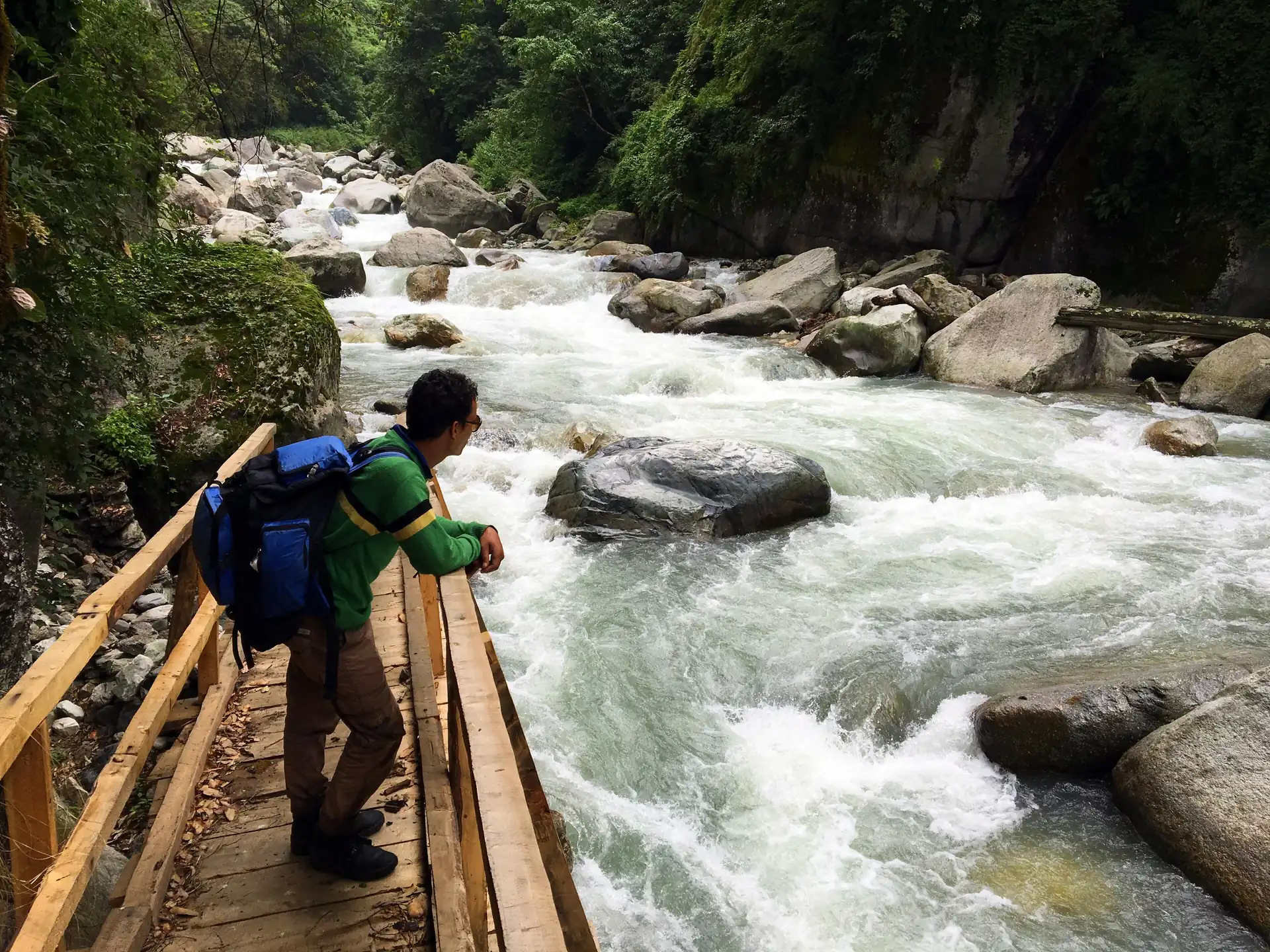 A walker on a wooden bridge above the Tirthan's rapids