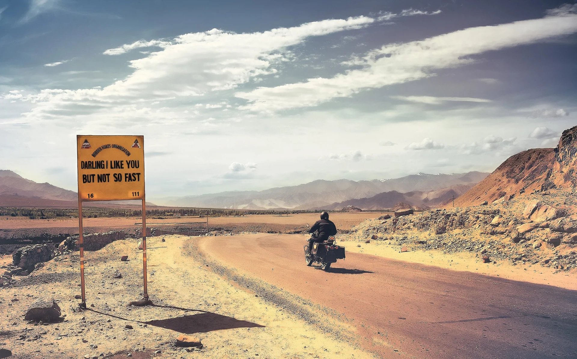 A rider passing a road sign on a high Ladakh road
