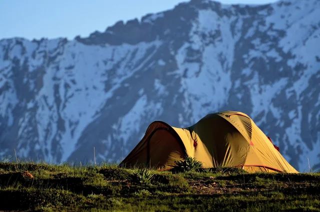A tent pitched on a ridge below snow mountains