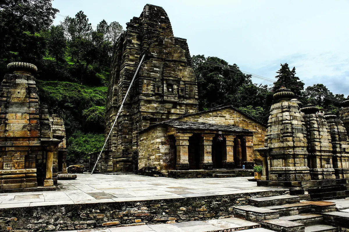 The tall stone tower of the Katarmal Sun Temple above a platform of small stone shrines, with forest behind