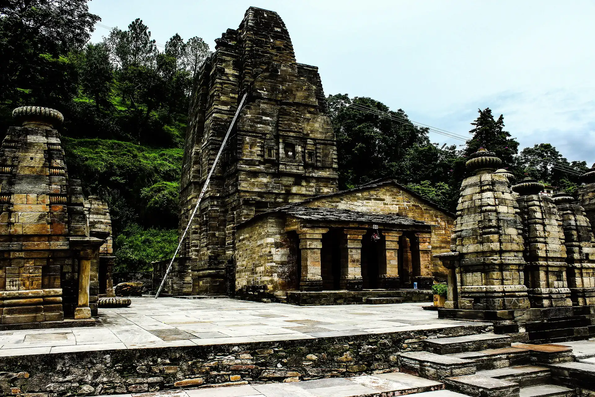 The tall stone tower of the Katarmal Sun Temple above a platform of small stone shrines, with forest behind