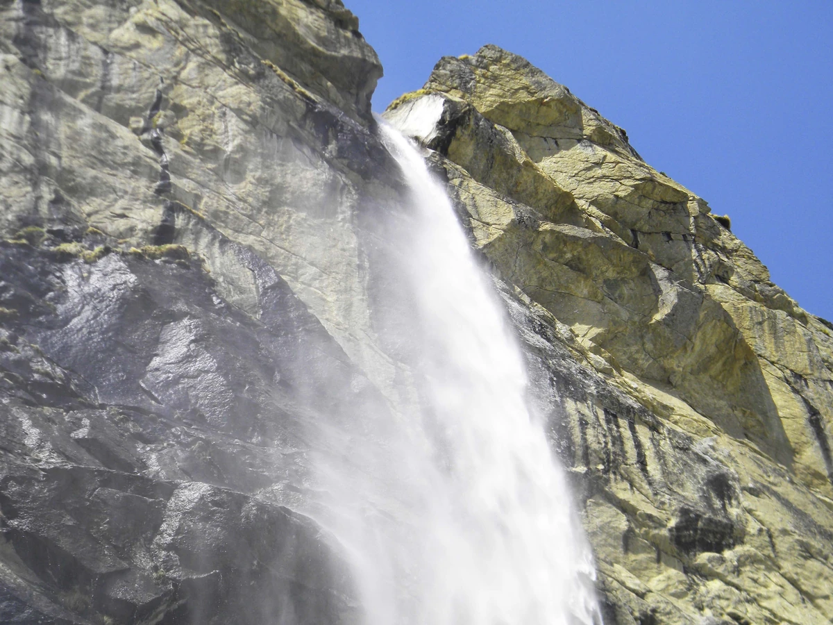 Vasudhara Falls dropping in a white stream down a sheer grey cliff against a blue sky