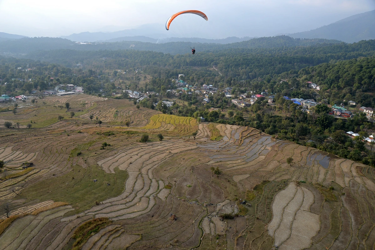 Bir from the air, with terraced fields, the village and a paraglider over the valley