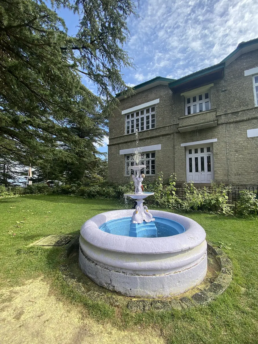 A white fountain on the lawn in front of the Chail Palace