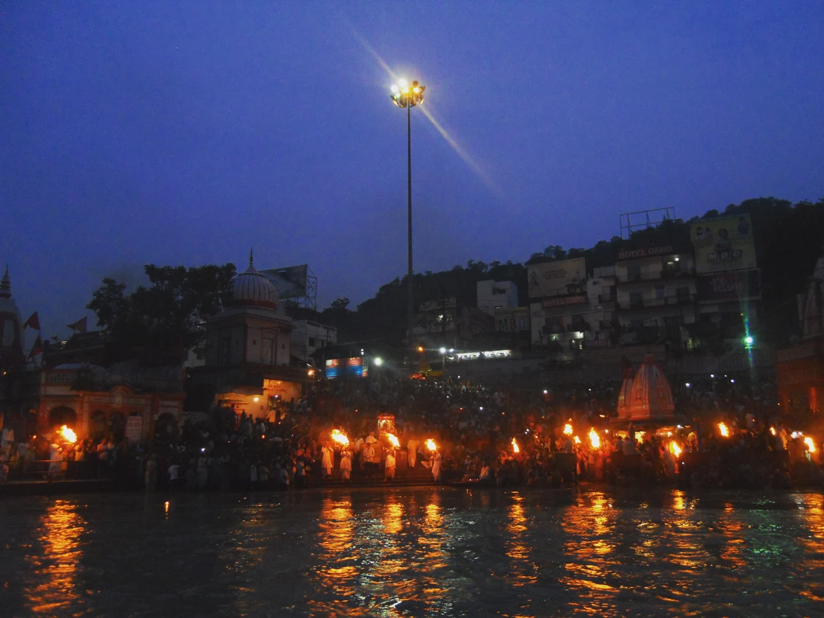 The ghat at Har Ki Pauri at dusk with rows of lamps lit along the water's edge under a blue evening sky