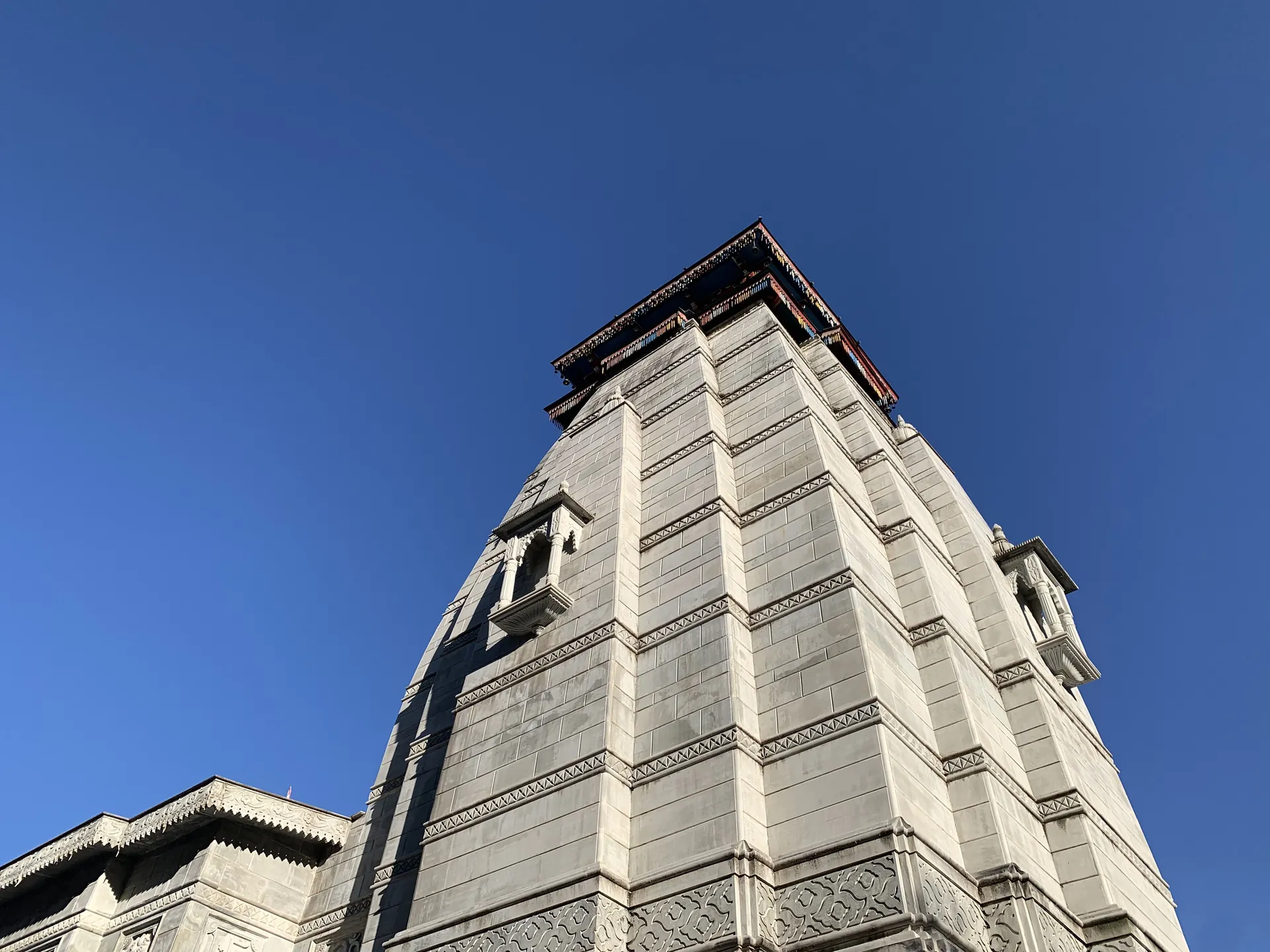 The tall grey stone tower of the Narsingh Temple in Joshimath, seen from below against a deep blue sky