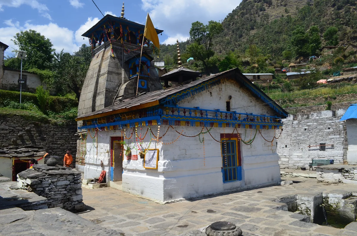 The small white and blue Triyuginarayan temple with a dark stone tower and a paved courtyard