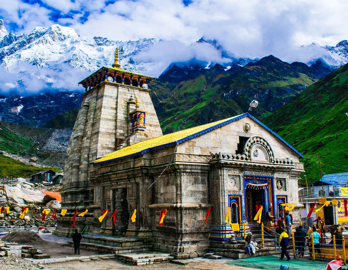 The Kedarnath Temple with a yellow roof below green slopes and snow-covered peaks