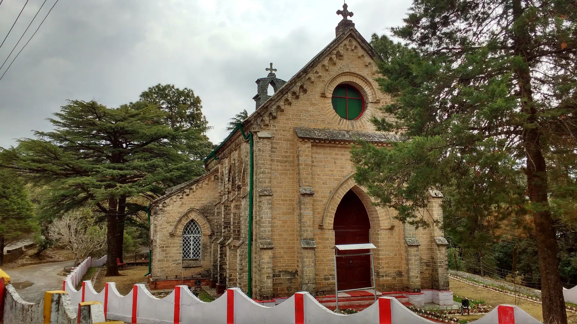 The stone Gothic front of St Mary's Church with a round window, a red door and tall deodars beside it