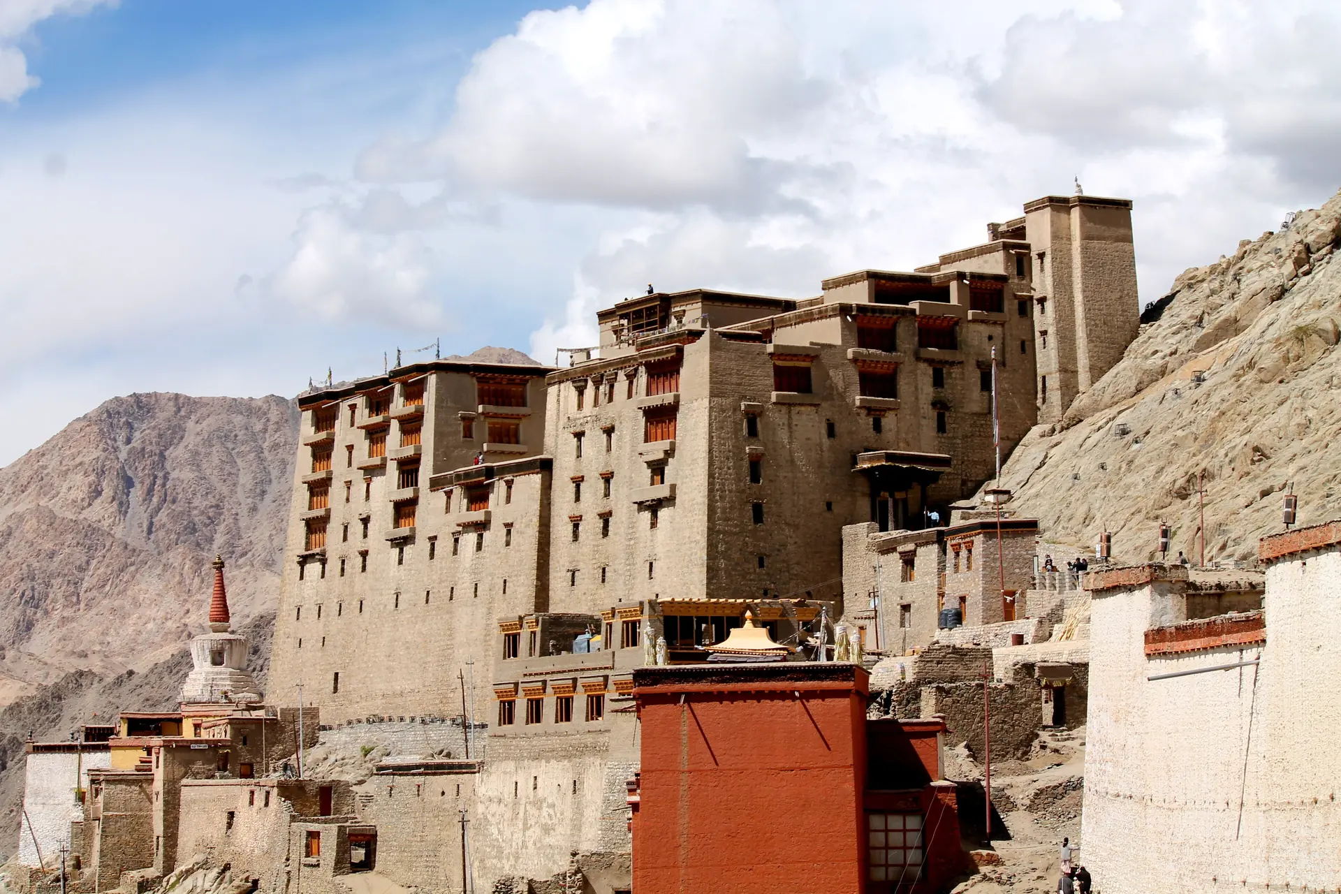 The stepped brown walls of Leh Palace on its rocky ridge under a blue sky with bare mountains behind