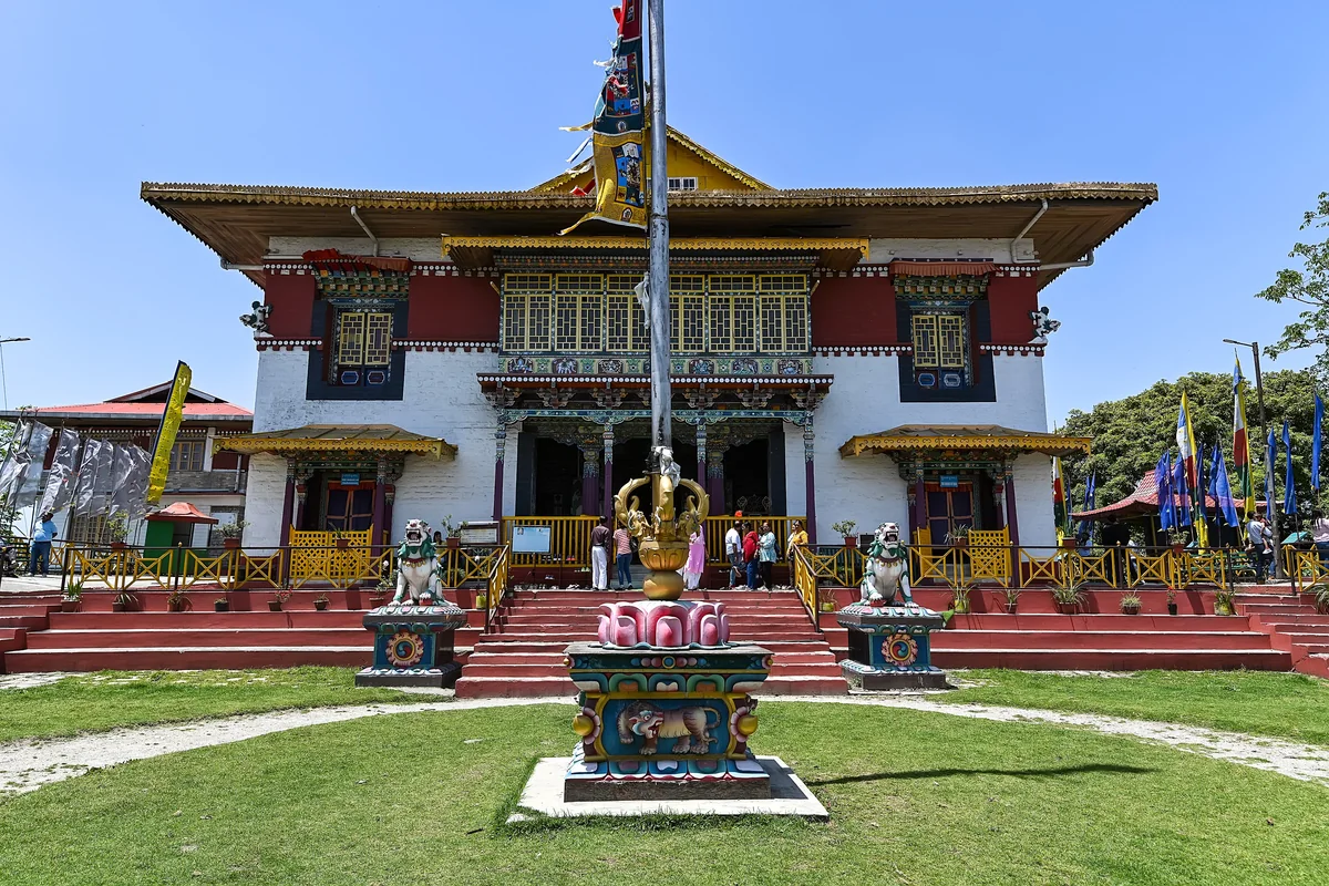 The white and red front of Pemayangtse Monastery with a flagpole and a green lawn under a clear sky