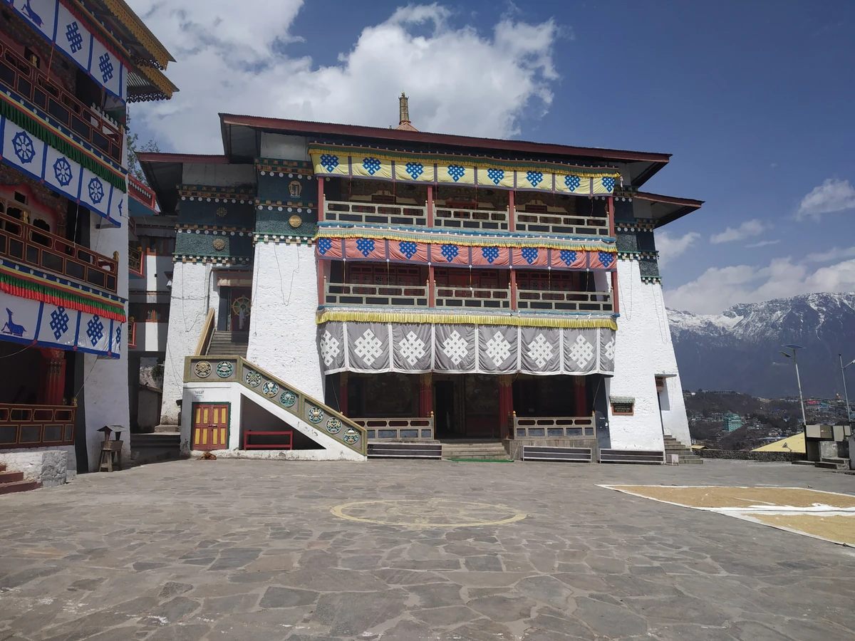 The painted three-storey front of the assembly hall of Tawang Monastery above a wide stone courtyard, with snow peaks behind