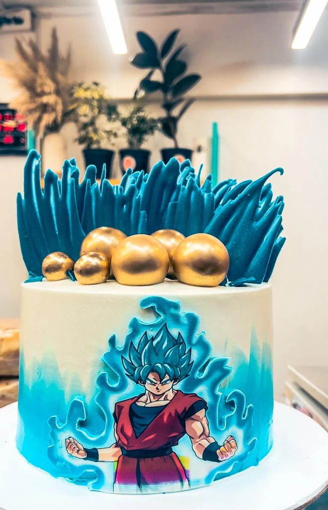 An anime cake with a painted hero and gold spheres