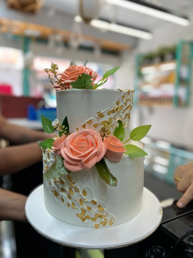 A two-tier white cake with sugar roses and gold leaf