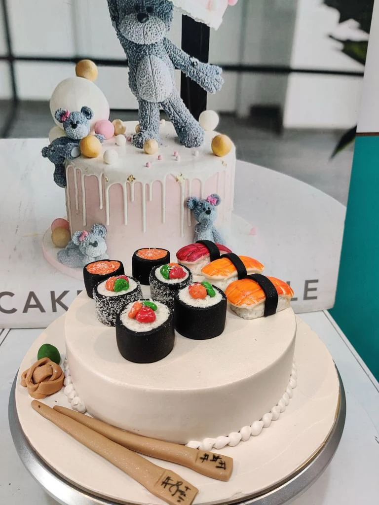A cake topped with sugar sushi and a teddy
