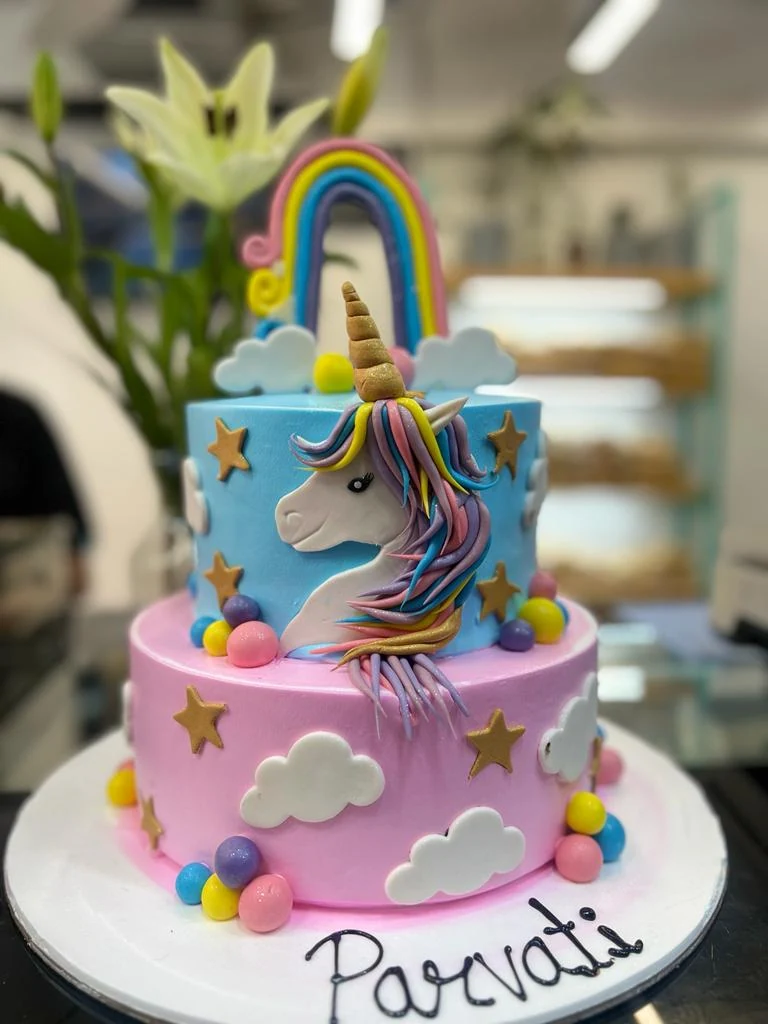 A two-tier unicorn cake with rainbow and clouds