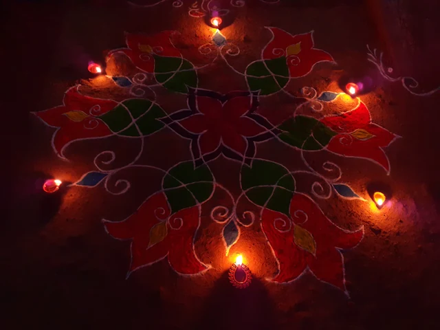 A bright rangoli of red flowers and leaves on the floor, ringed with small lit clay lamps in the dark