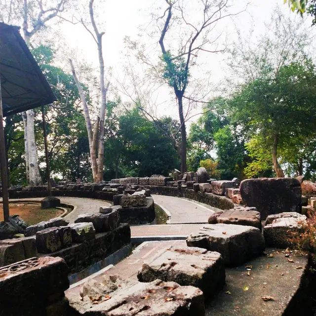 Weathered stone blocks and a sunken stone platform among trees at the Deopahar archaeological site