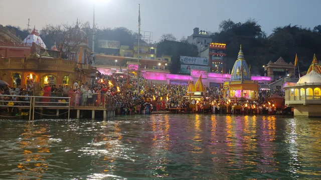 Crowds on the steps of the Haridwar ghats at dusk, with lit shrines along the bank and the Ganga in the foreground