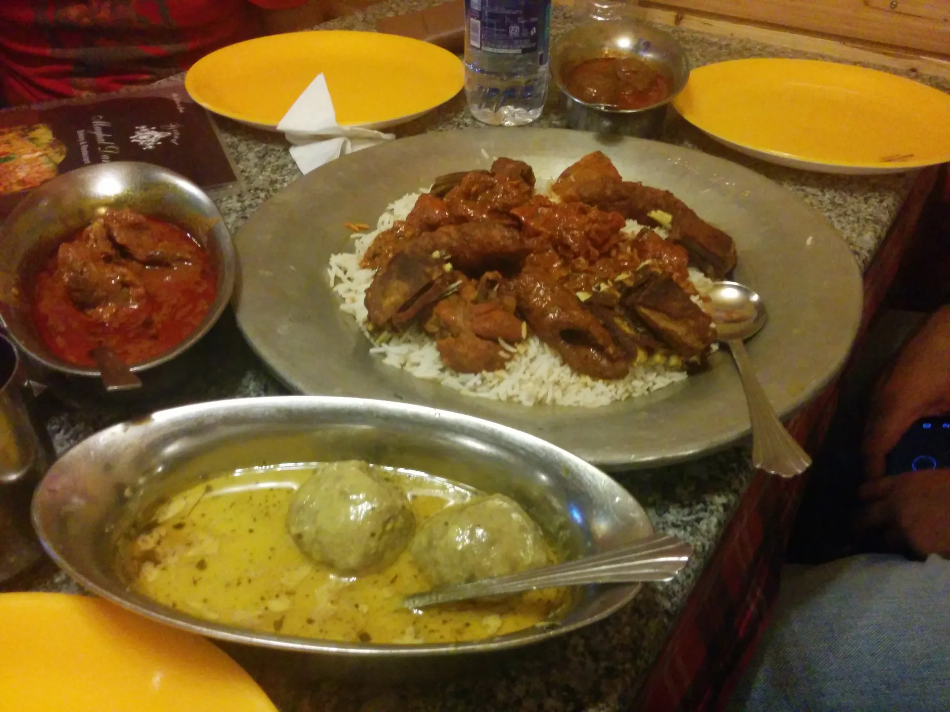 A wazwan meal laid out on a metal tray, with rice, meat dishes, a bowl of yellow gravy with meatballs and small dishes of sauce