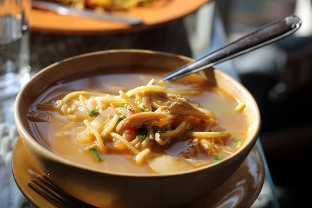 A bowl of thukpa, a noodle soup with shredded meat and herbs, with a spoon resting in it