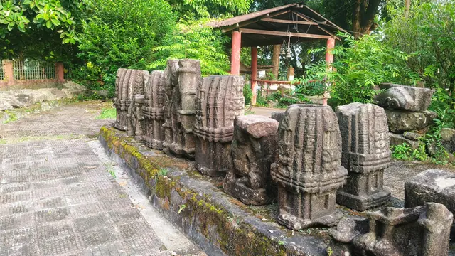 A row of carved stone temple blocks under a small shelter on a paved terrace among trees
