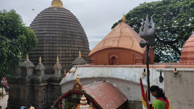 The tall dark beehive-shaped dome of Kamakhya Temple above smaller red domes and a trident among trees