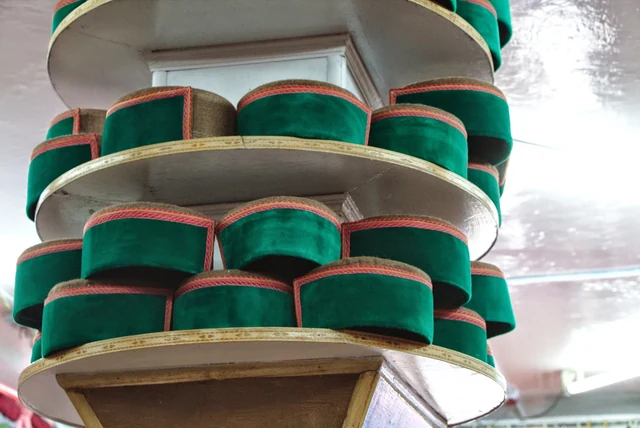 Stacks of woollen Himachali caps with green velvet bands on shelves in a shop