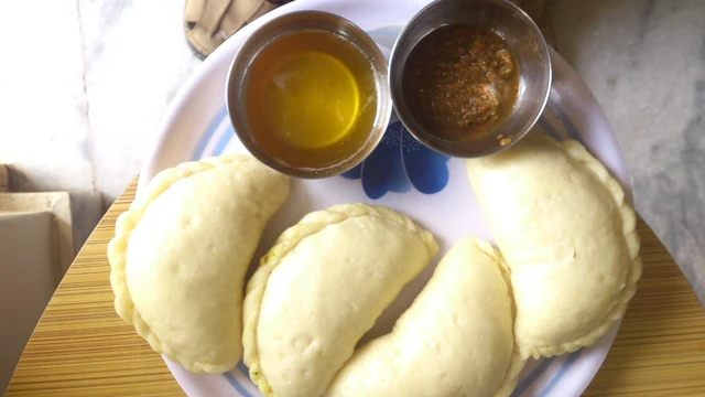 Steamed stuffed siddu buns on a plate with small bowls of ghee and chutney