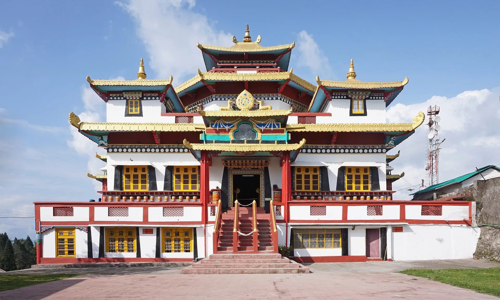 The three-tiered white and red front of Zang Dhok Palri Phodang monastery with gold roof edges under a blue sky with clouds