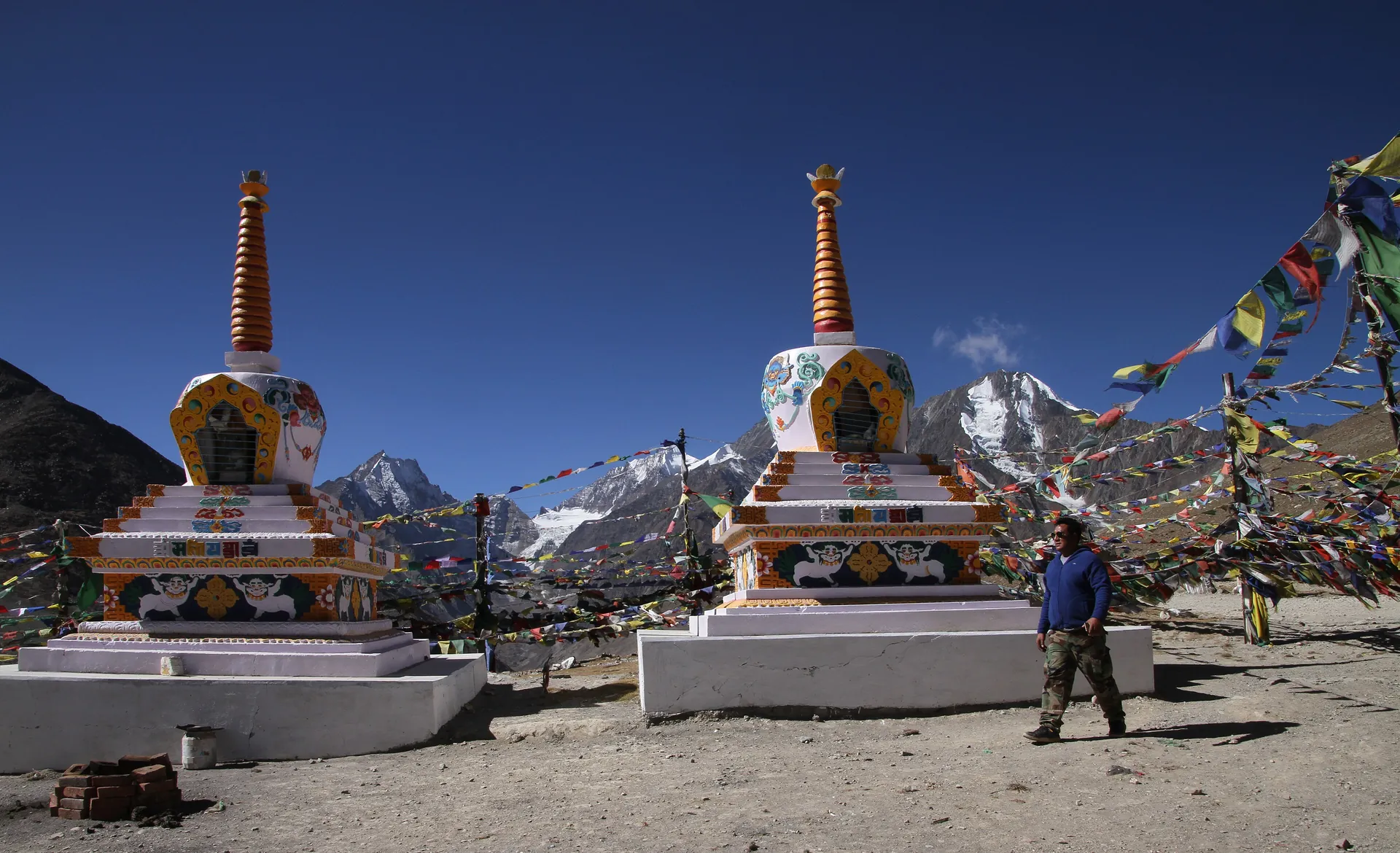 Two whitewashed chortens with prayer flags on Kunzum Pass under a deep blue sky