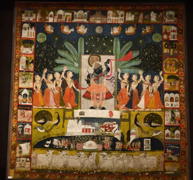 A painted temple cloth with Krishna in the middle, women dancing around him and a full moon in a night sky