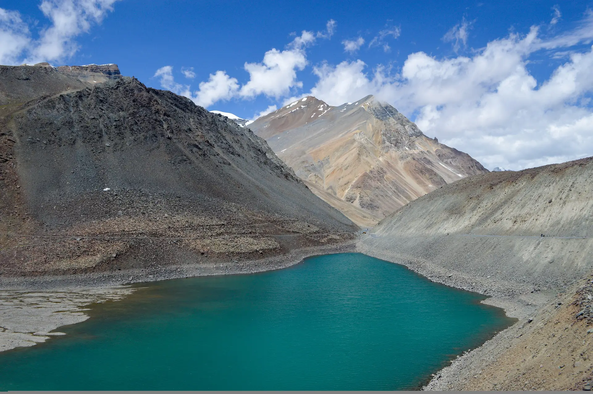 The turquoise water of Suraj Tal below bare rock slopes under a blue sky