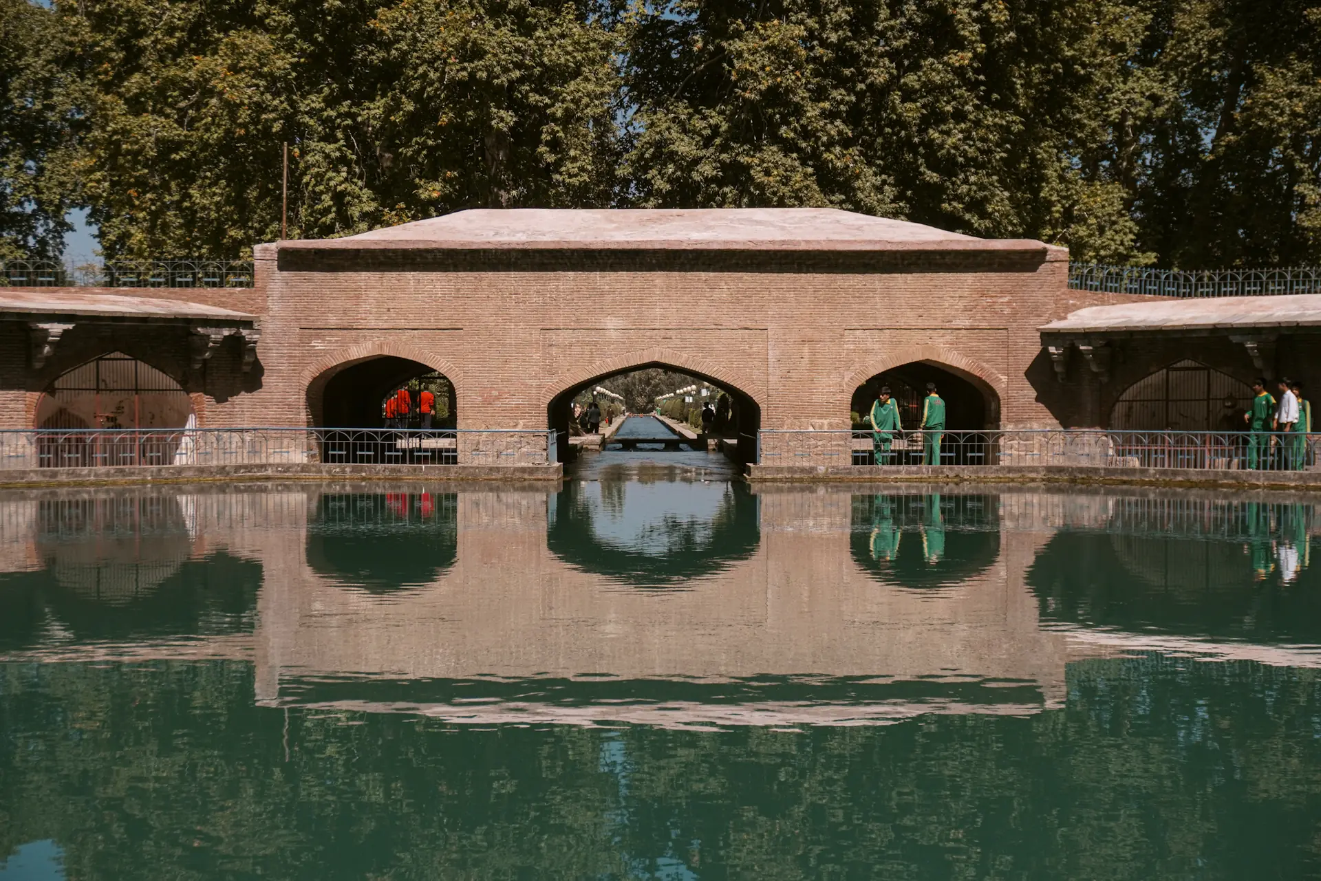 The arched Mughal arcade around the Verinag spring, reflected in still green water, with chinar trees behind