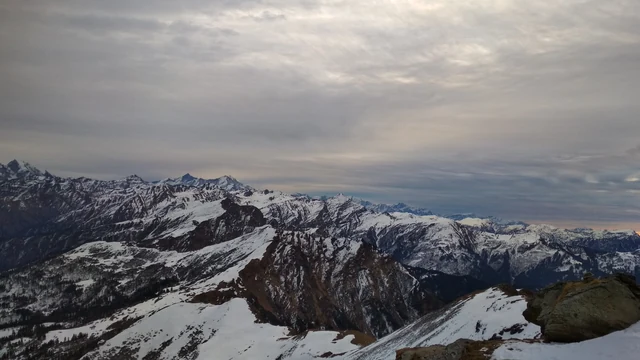 Snow-covered ridges and peaks of the Garhwal Himalaya under a grey sky, seen from the summit of Kedarkantha