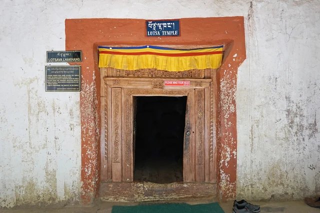 A low whitewashed doorway with an orange frame, a gold-and-yellow lintel cloth and two small signs on the wall
