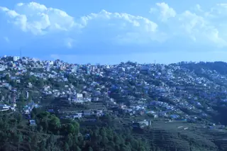 The town of Almora spread across a terraced ridge under a blue sky with clouds