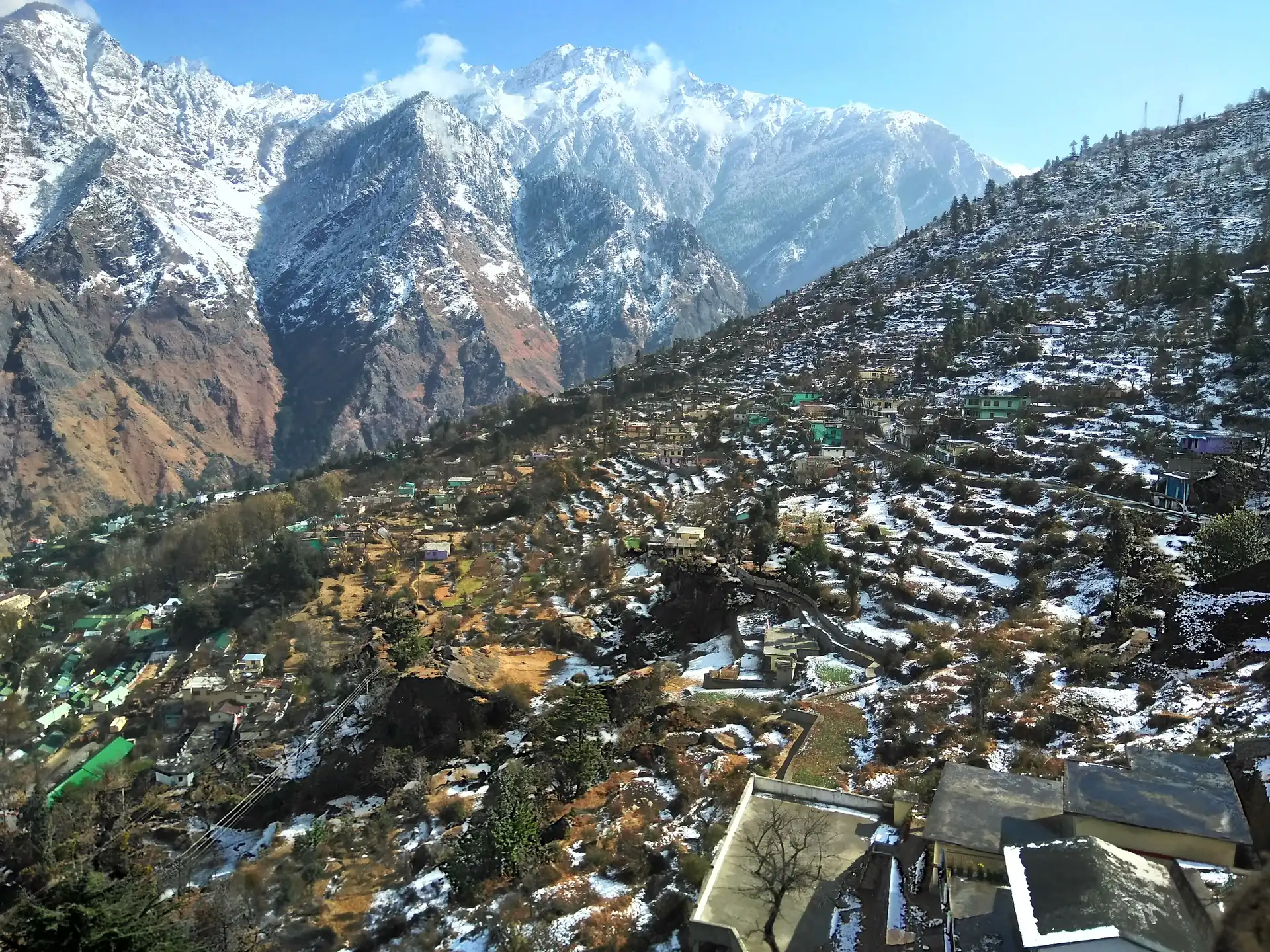 Snow-dusted terraced slopes at Auli with high snow peaks rising across the valley under a blue sky