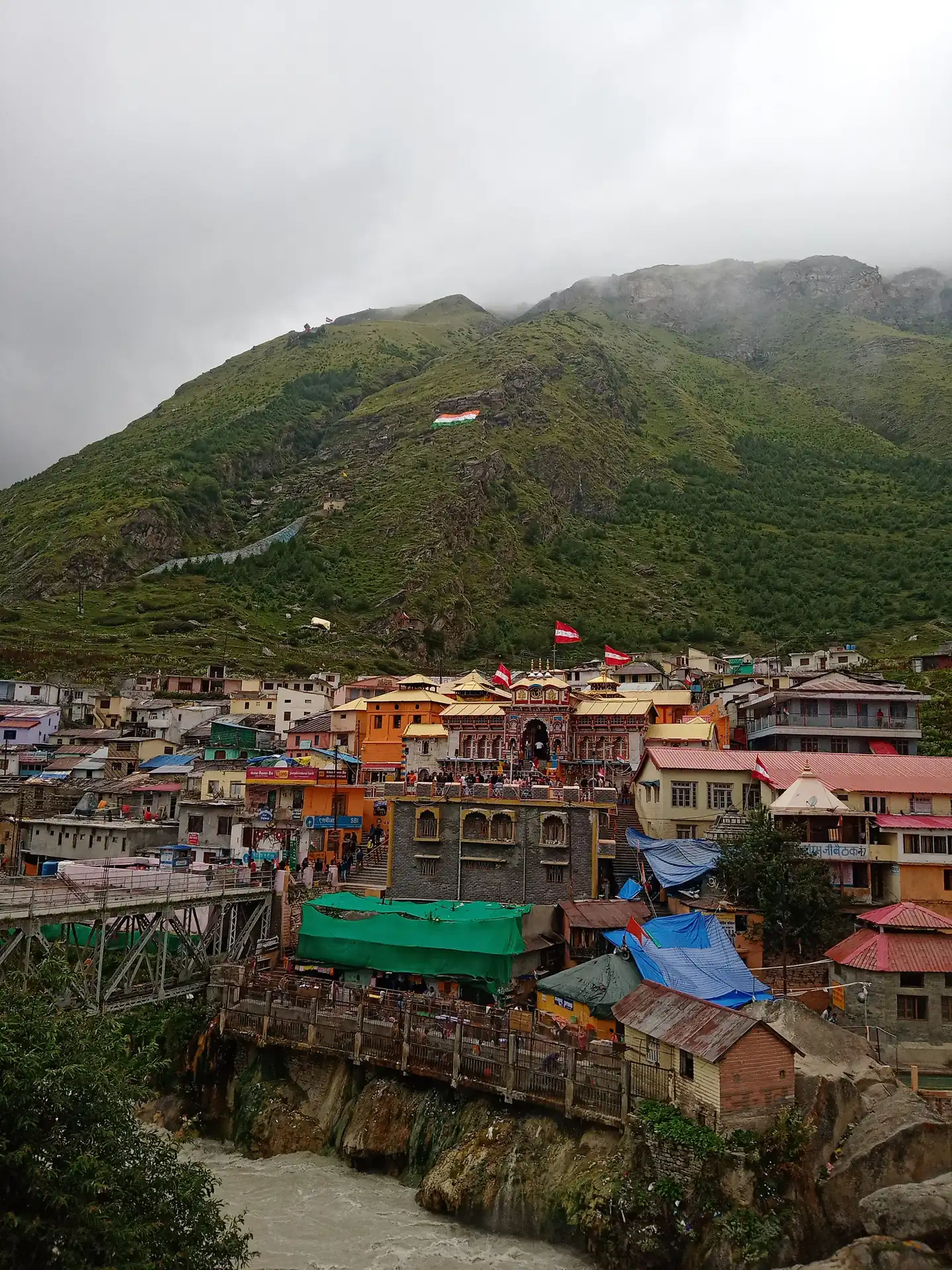 Badrinath town with the temple in the centre and the Tapt Kund hot springs above the river bank, green slopes behind