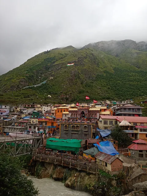Badrinath town with the temple in the centre and the Tapt Kund hot springs above the river bank, green slopes behind