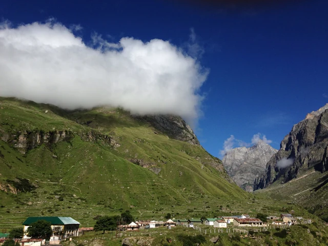 The low houses of Mana village on a green slope below steep rock walls and drifting cloud