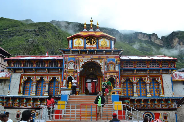 The front of the Badrinath Temple, a painted stone façade with arched windows and a gilt cupola, a stairway leading up to it