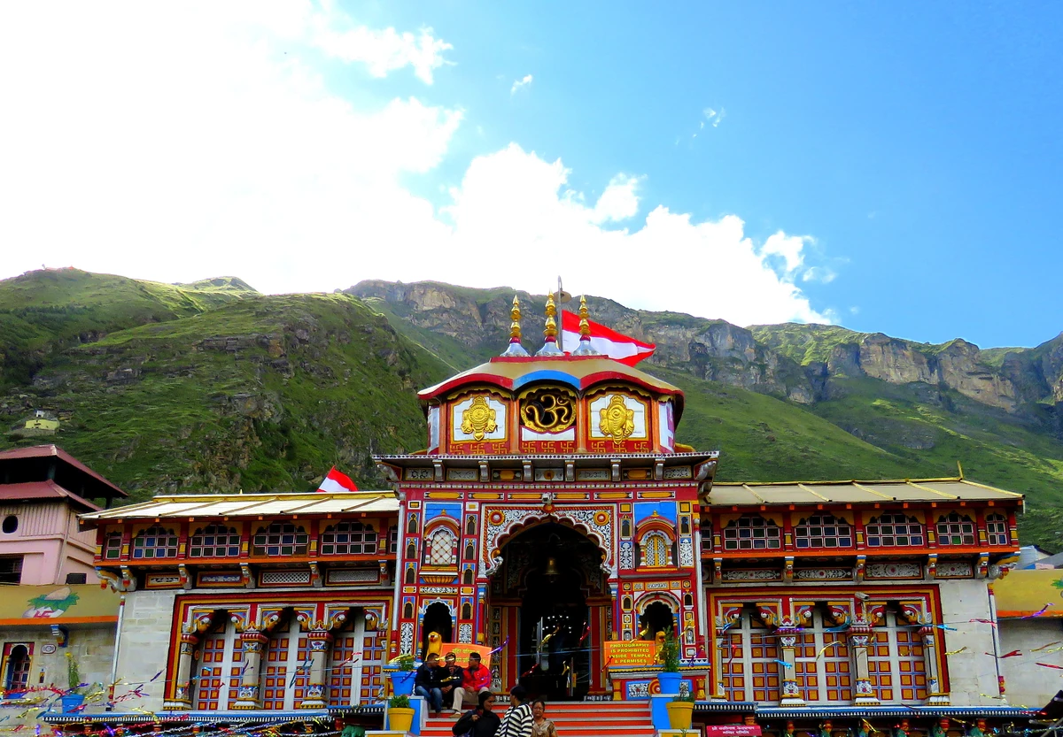 The painted stone façade of the Badrinath Temple with its gilt cupola, under green slopes and a blue sky