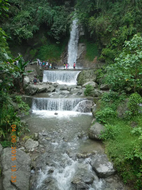 A tall, narrow waterfall dropping through green forest into stepped rock pools at Banjhakri Falls