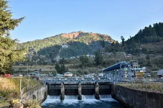 The gates of the Uhl barrage at Barot with water flowing out and forested hills behind