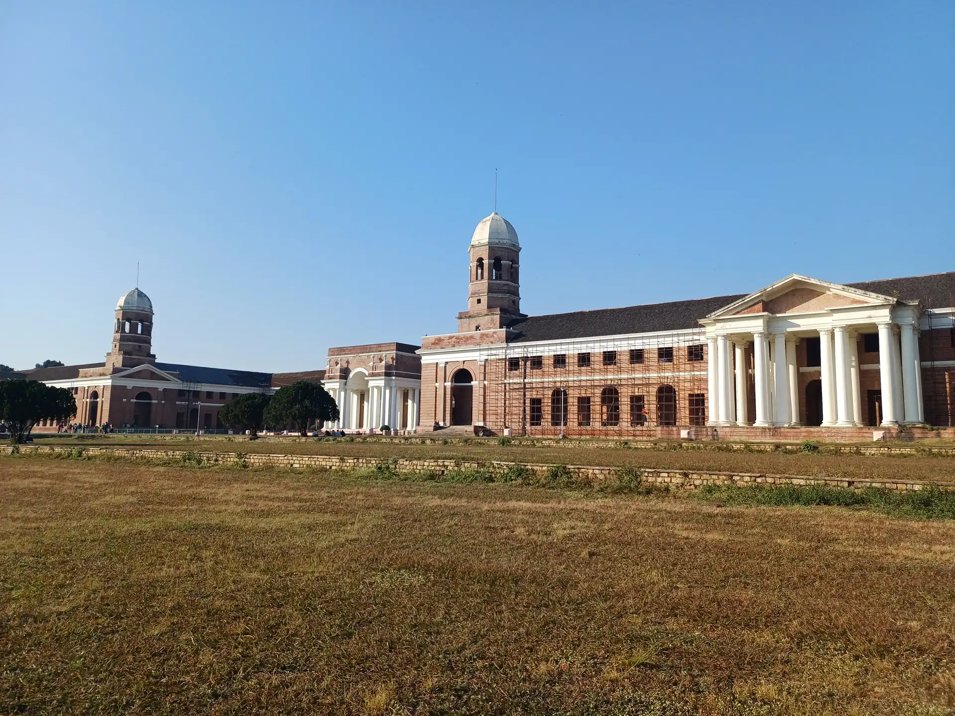 The Forest Research Institute's long red-brick front seen across a dry lawn under a clear blue sky