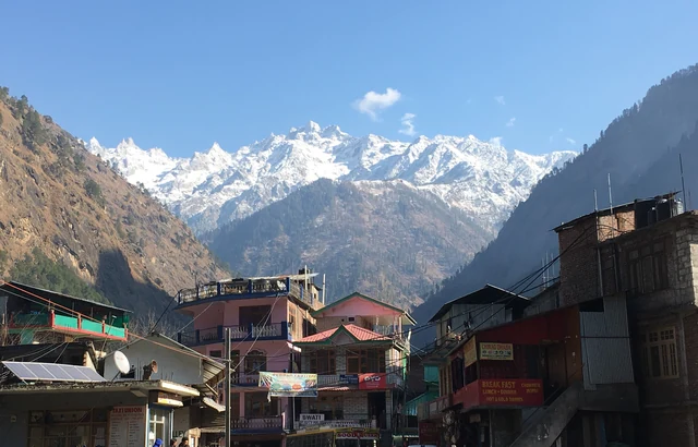 Snow peaks above the houses of Kasol under a clear sky