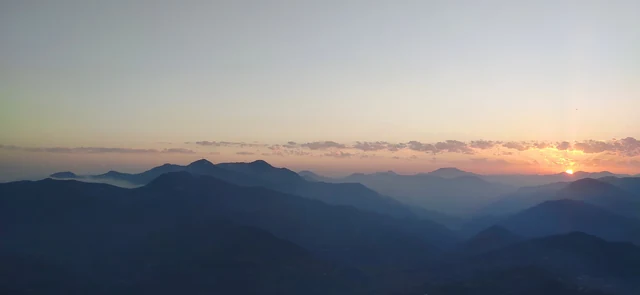 A wide orange glow along the horizon above layered dark ridges at dusk from Mukteshwar