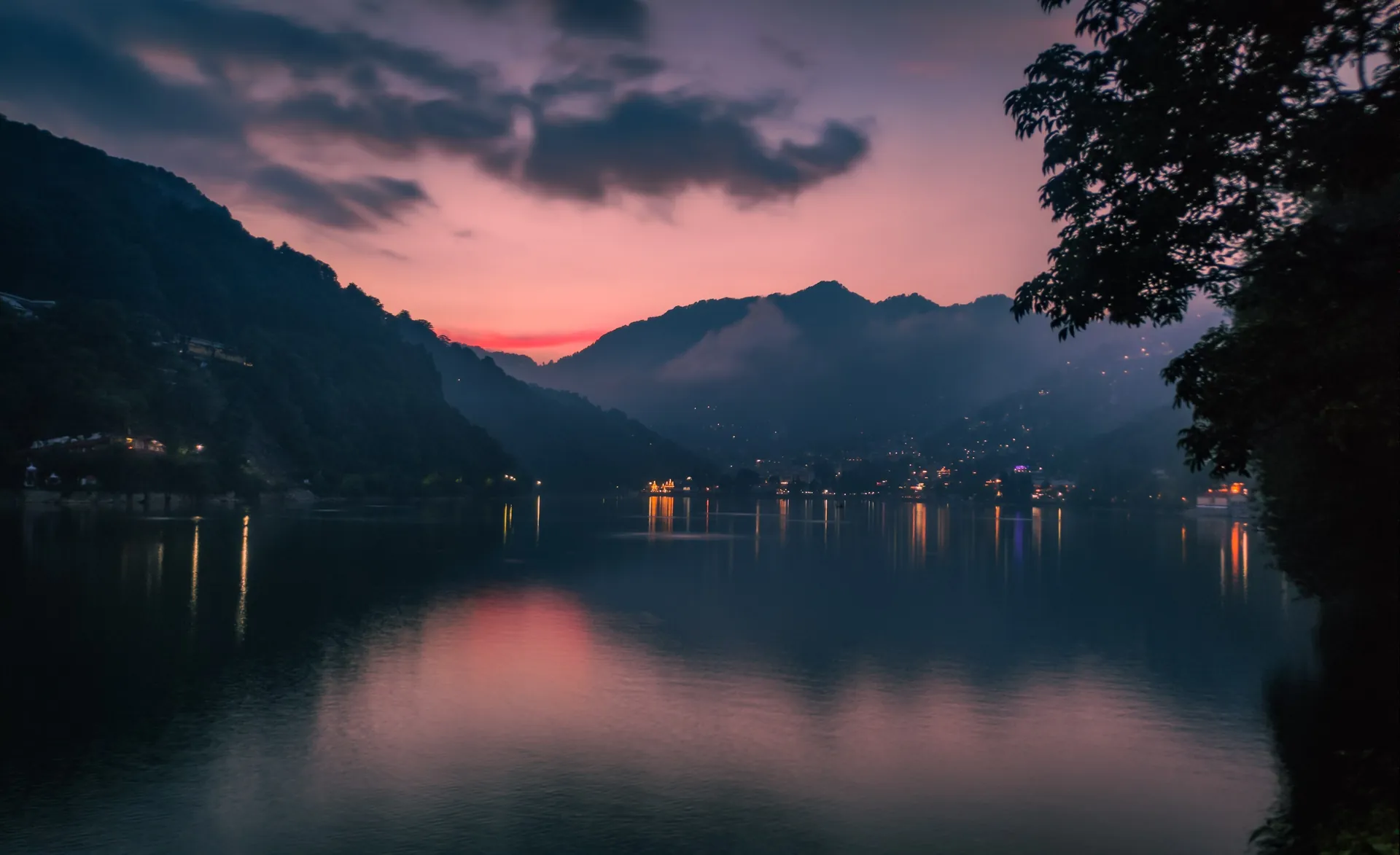 Nainital Lake in the evening under a pink sky, with the town lights on the far shore and dark hills behind
