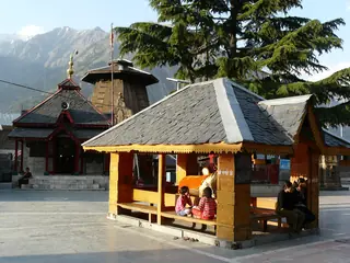 The courtyard of the Chaurasi temple complex with a wooden shelter and mountains behind